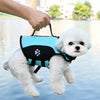 A white poodle wearing a blue life jacket is being held by a person over water.