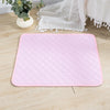 A pink hexagonal reusable washable pet training mat placed on a light wooden floor next to white lace fabric.