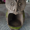A carved wooden owl bird feeder with a hollow body and green moss accents sits on a blue mesh surface.