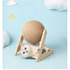 A small gray kitten is resting on a wooden base that holds a large, round sisal rope ball toy.