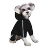 A small, light-colored dog wearing a black waterproof raincoat with a hood and reflective features.