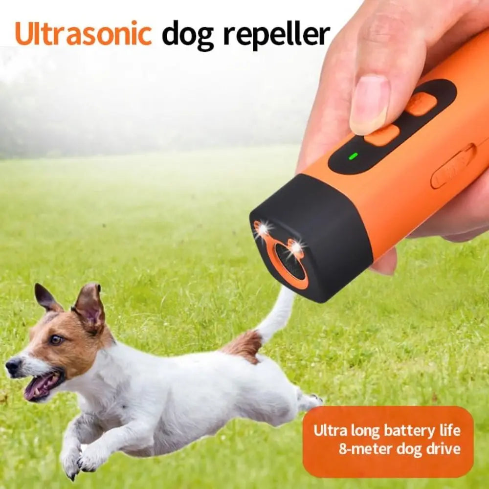 A hand holds an orange ultrasonic dog repeller device aimed at a dog running on green grass.