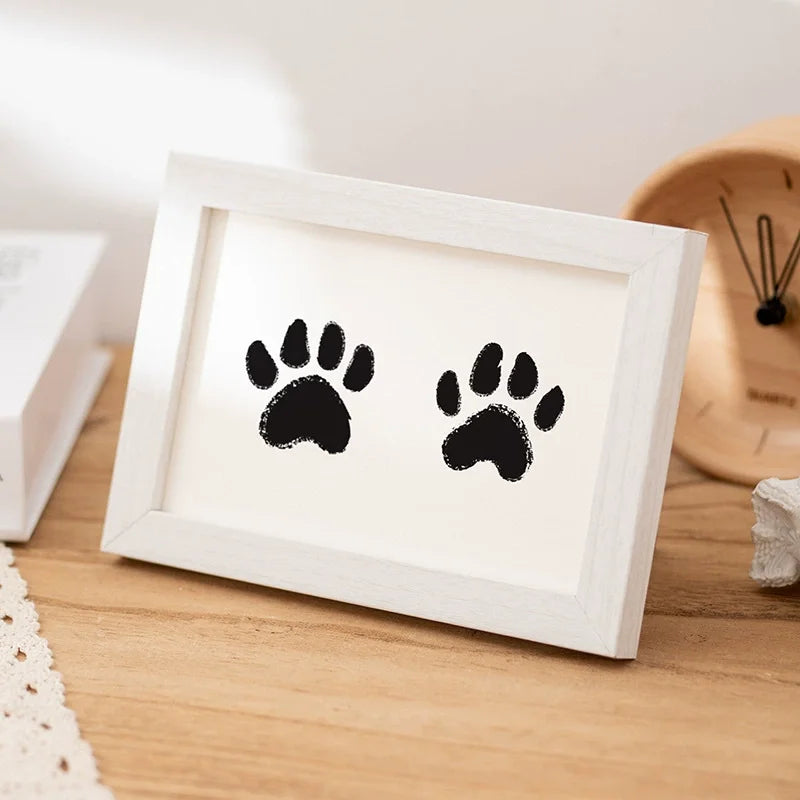 A white wooden photo frame displaying two black paw prints, suitable for a keepsake kit.
