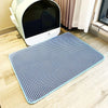 Un tapis de litière en maille bleue est placé sur un plancher en bois clair devant une boîte à litière pour animaux blanche.