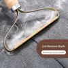 A manual lint remover brush with a wooden handle and gold-colored metal frame is shown against a gray fabric background.