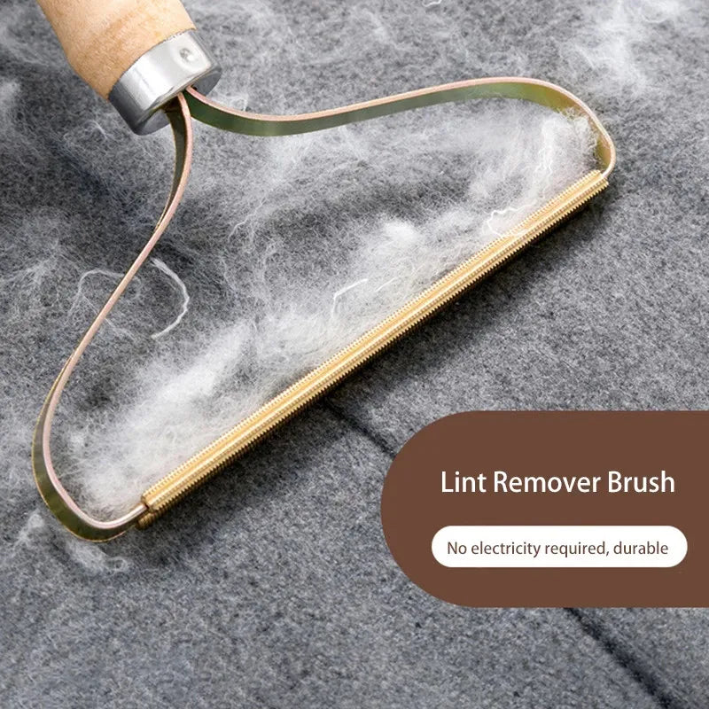 A manual lint remover brush with a wooden handle and gold-colored metal frame is shown against a gray fabric background.