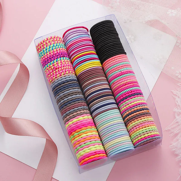 A clear box filled with colorful elastic hair bands in various shades of pink, purple, blue, and green.