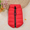 A bright red padded dog coat jacket with a black zipper and silver ring detail resting on a light fabric surface.