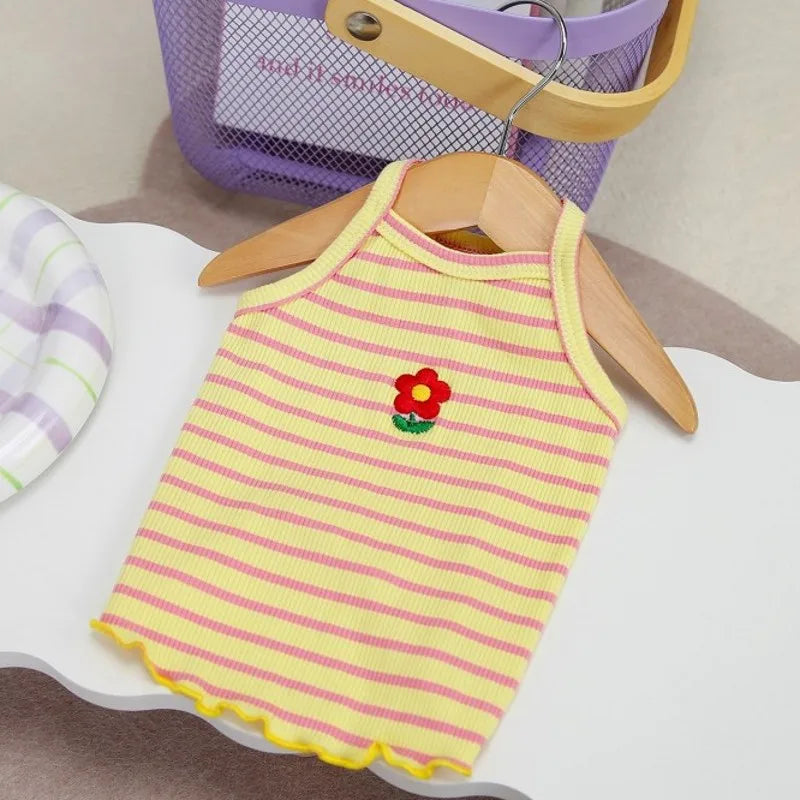 A yellow and pink striped dog vest with a red flower detail is displayed on a white surface.