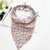 A pink and blue floral paisley triangle scarf laid on white paper with white roses.