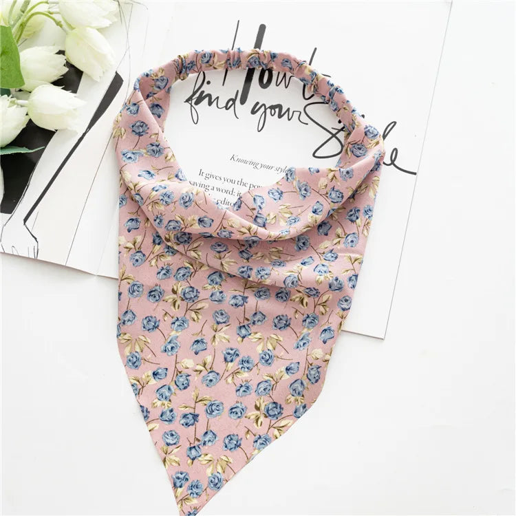 A pink and blue floral paisley triangle scarf laid on white paper with white roses.