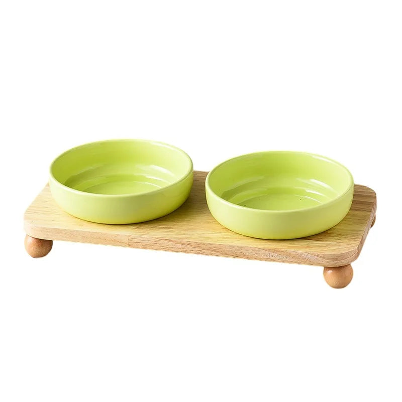 A light green ceramic cat and dog bowl set with a wooden stand.