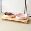A pink ceramic cat and dog bowl is placed on a wooden stand with a pile of dry food.