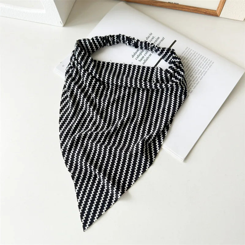 Diadema o pañuelo elástico con estampado geométrico en blanco y negro, sobre un libro blanco.