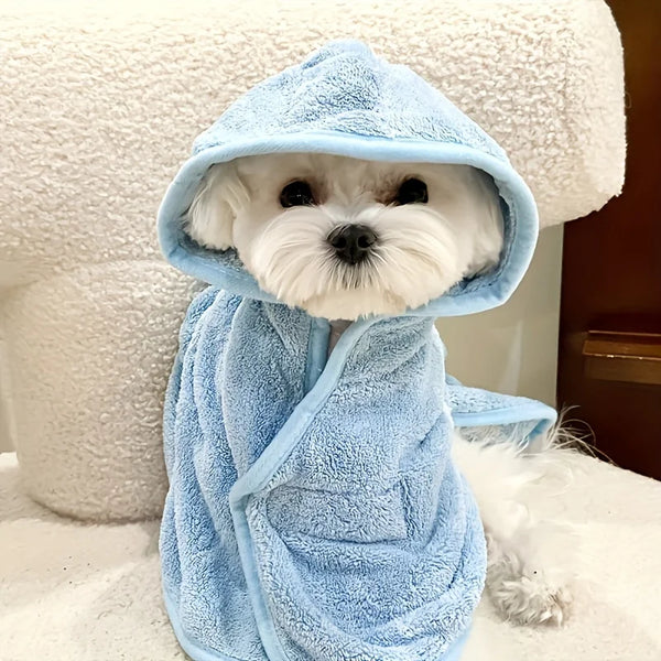 A white dog wearing a light blue absorbent quick-dry bathrobe, sitting on a white surface.