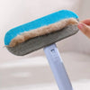A hand is holding a silicone pet hair removal brush with blue and gray bristles and a white handle.