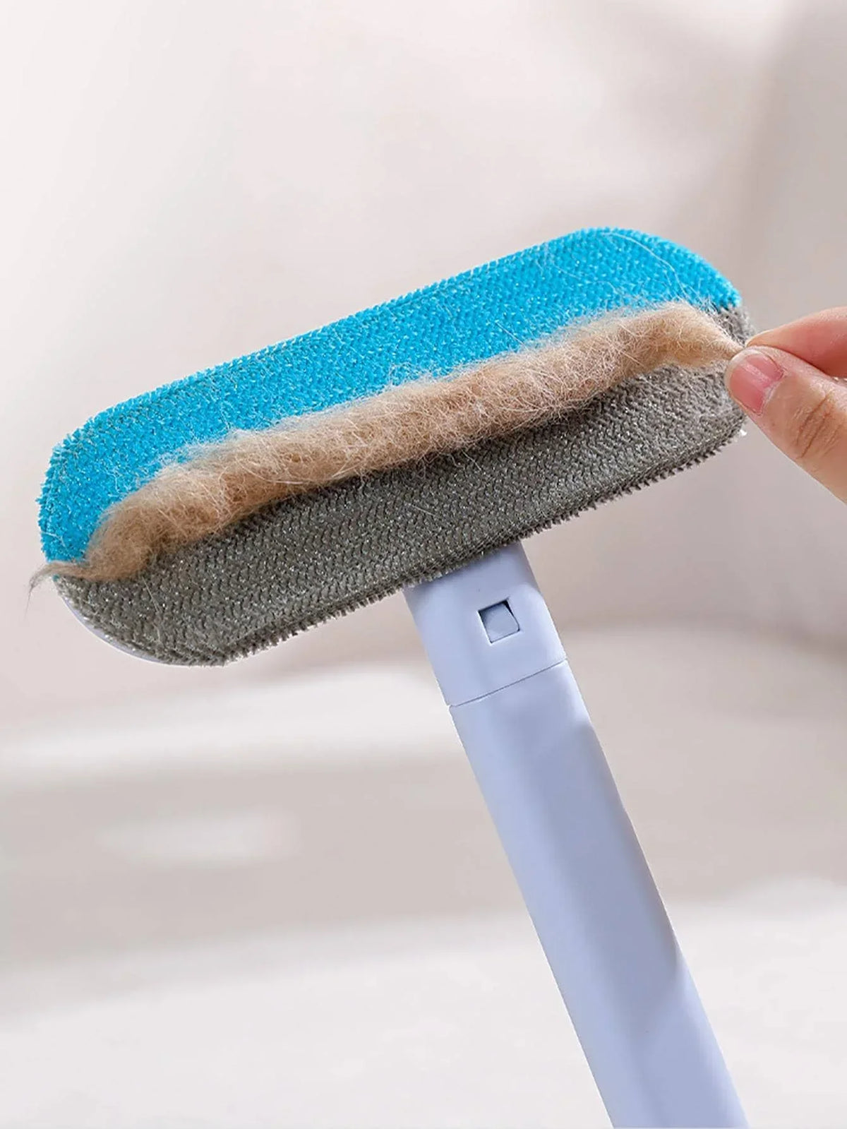 A hand is holding a silicone pet hair removal brush with blue and gray bristles and a white handle.