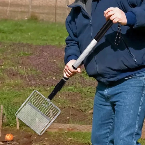 A person is using a black and silver stretchable stainless steel poop scooper to clean up in an outdoor area.