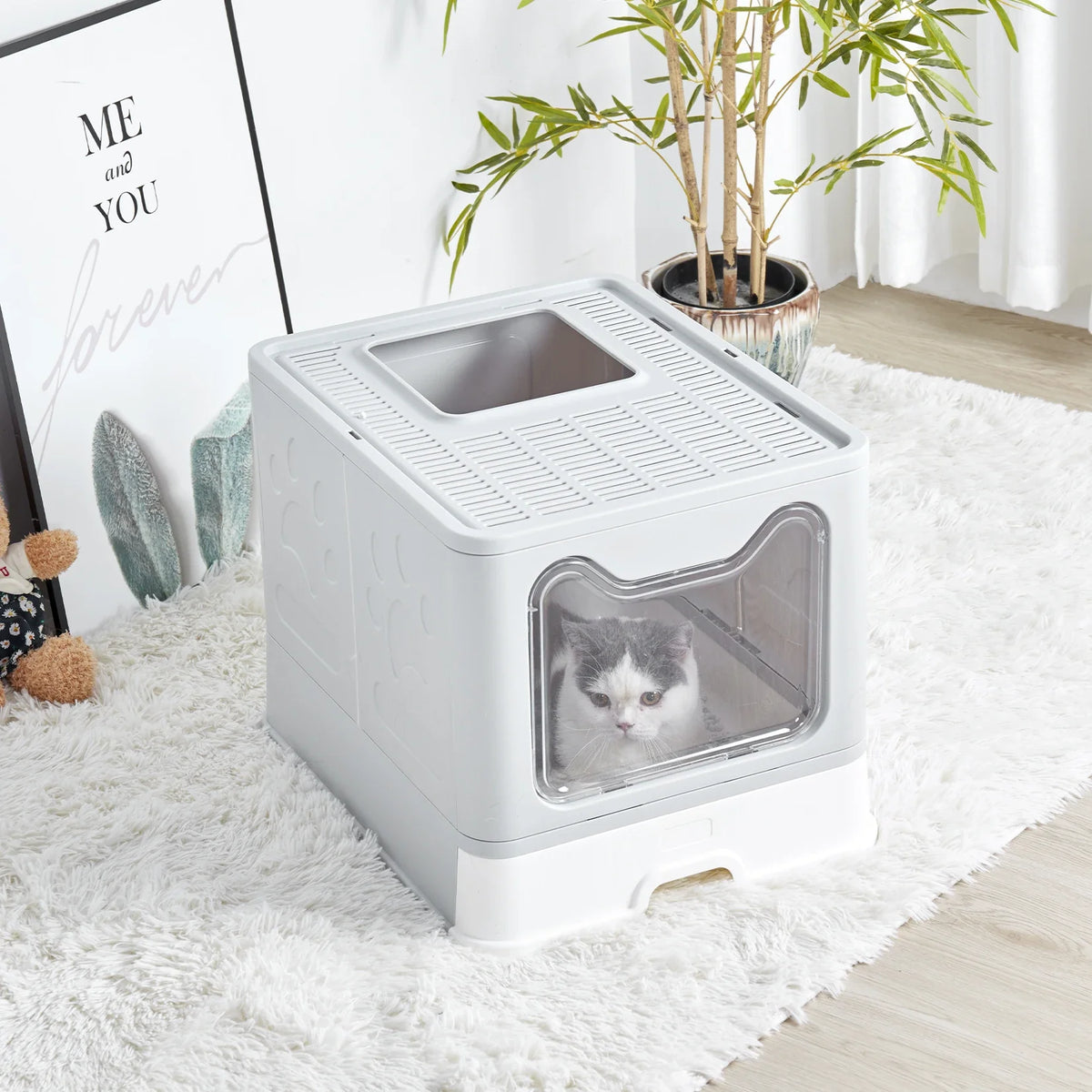A white foldable cat litter box with a front entry and top exit is placed on a fluffy white rug.