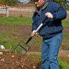 A man is using a long-handled stainless steel tool to scoop material in an outdoor setting.