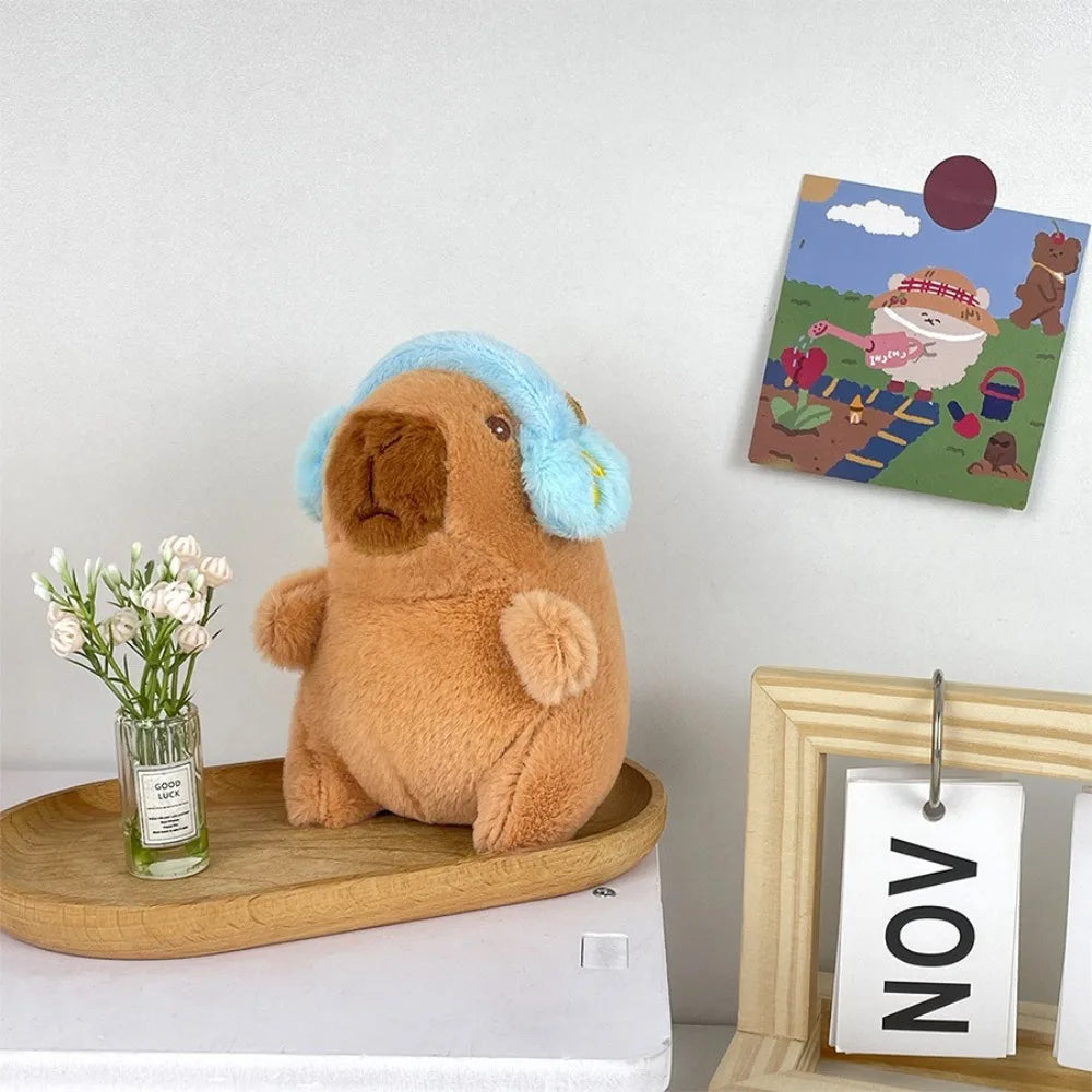 A brown capybara plush toy with light blue accents sits next to a framed illustration of a capybara.