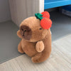 A brown capybara plush doll with green leaves and orange wings sitting on a light wooden surface.