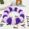 A purple and pink fluffy pet collar and bow tie set lying on a white surface.