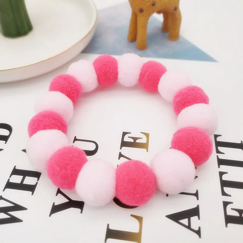 A bracelet made of pink and white fuzzy pom-poms, set with a yellow giraffe toy.