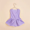 A purple polka dot dog dress for small breeds with a gathered skirt, displayed on a hanger.