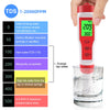 A hand holds a red digital water quality meter measuring TDS levels in a glass of water.