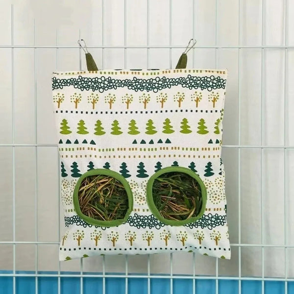 Un sac à foin en toile avec fond blanc, motifs d'arbres verts et bruns et ouvertures circulaires pour la nourriture des anima