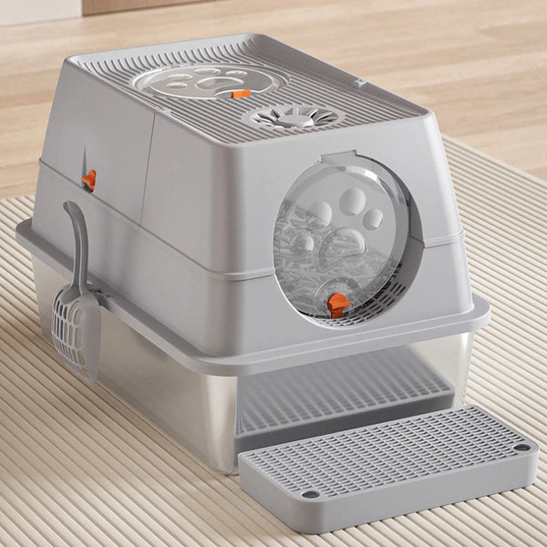 A gray fully enclosed stainless steel cat litter box with a flip-top lid resting on a light wooden surface.