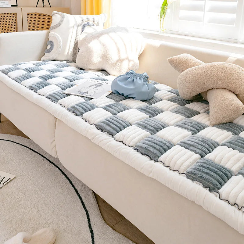 A plush fleece pet bed and mat featuring gray, white, and light blue patterned fabric on a cream sofa.