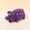 A purple pig-shaped squeaky toy with pink polka dots resting on a white surface.