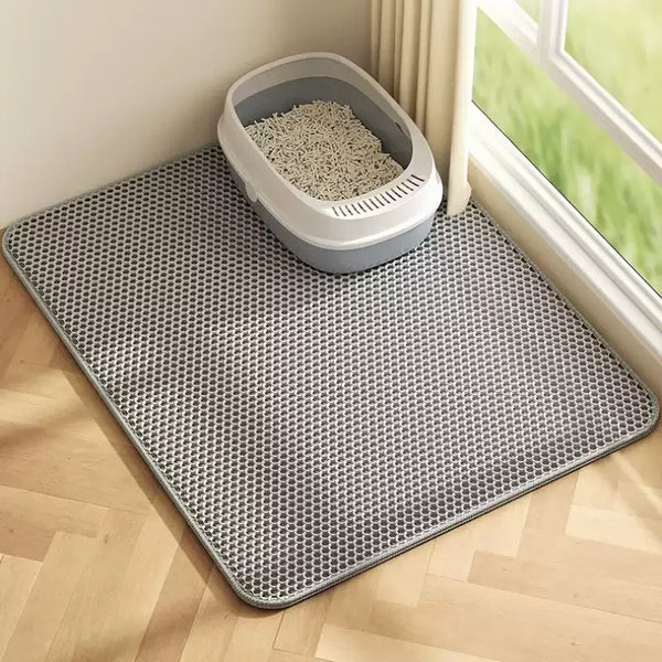A gray waterproof double-layer cat litter mat with a removable tray is placed on a light wooden floor near a window.