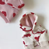 Sudadera blanca con estampados de corazón rojo y acentos rosa, doblada sobre una superficie blanca.