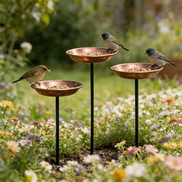 A decorative metal bird feeder station with four shallow bowls planted in a garden setting.