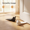 A black cat figurine is placed next to a white cat figurine on a wooden floor near a door frame.
