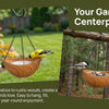 A wooden bird feeder with a bowl is hanging from an iron chain in a garden setting.