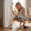 A woman is kneeling on a wooden floor next to a white door, with a black cat and a white wedge visible.